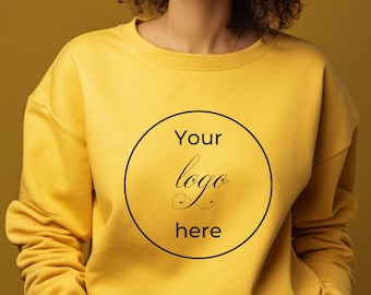 May include: Mustard yellow sweatshirt with a crew neck. A black circle with the words "Your logo here" is printed on the front. The sweatshirt is made of a soft material.
