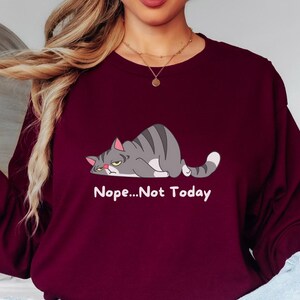 Women’s cozy crewneck sweatshirt with funny grumpy cat design, ideal for everyday comfort, relaxed weekends, and casual outfits.  A sweatshirt with a cartoon gray cat lying down with the text 'Nope...Not Today' printed below the cat.
