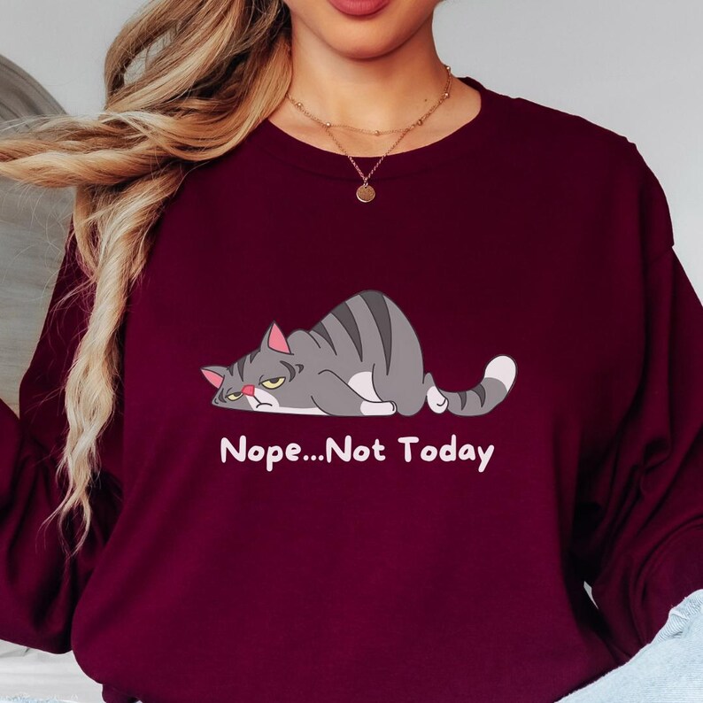 Women’s cozy crewneck sweatshirt with funny grumpy cat design, ideal for everyday comfort, relaxed weekends, and casual outfits.  A sweatshirt with a cartoon gray cat lying down with the text 'Nope...Not Today' printed below the cat.