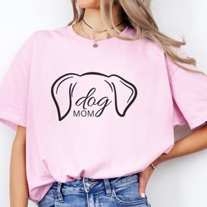 T-Shirt featuring a minimalist design with dog ears and the phrase 'dog MOM' in cursive, perfect for dog lovers who want to showcase their love for their pets in a stylish and comfortable way.