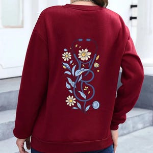 May include: A sweatshirt with a blue stethoscope and floral design on the back.