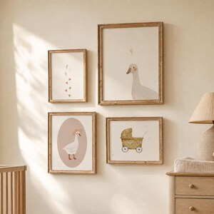 Op de afbeelding: Vier ingelijste wandprints met illustraties van een gans, ganzenvoetsporen en een rieten kinderwagen. De prints zijn ingelijst in licht houten lijsten aan een neutrale muur boven een houten wieg en een dressoir met een lamp en een knuffeldier.