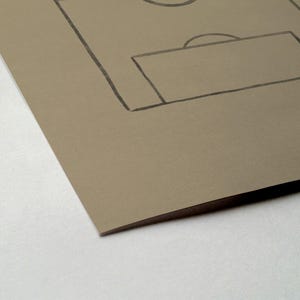 May include: A sketch of a soccer field on tan paper. The field's lines and goal are drawn in black. The paper is angled, showing a corner and the edge of the paper.