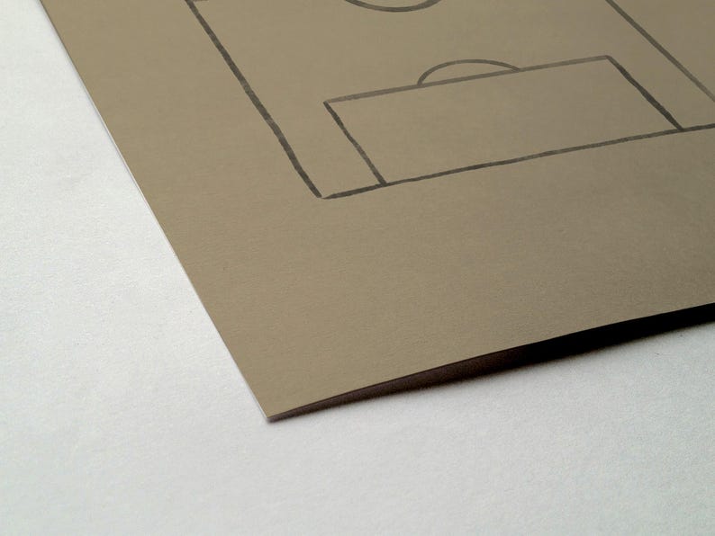 May include: A sketch of a soccer field on tan paper. The field's lines and goal are drawn in black. The paper is angled, showing a corner and the edge of the paper.