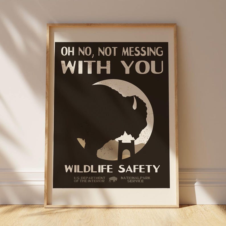 May include: A framed poster with a wildlife safety theme. The poster features a black background with white text that reads "OH NO, NOT MESSING WITH YOU" and "WILDLIFE SAFETY." A white bison silhouette is in the center. The bottom of the poster includes the US Department of the Interior and National Park Service logos.