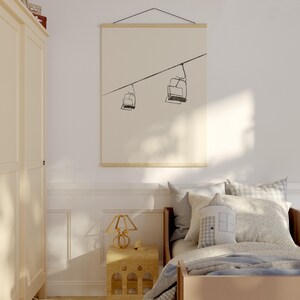 May include: A framed print with a minimalist line drawing of two ski lift chairs on a cable. The artwork is displayed on a light background, adding a touch of modern decor to a bedroom. The print is hung with wooden bars, creating a simple, elegant look.