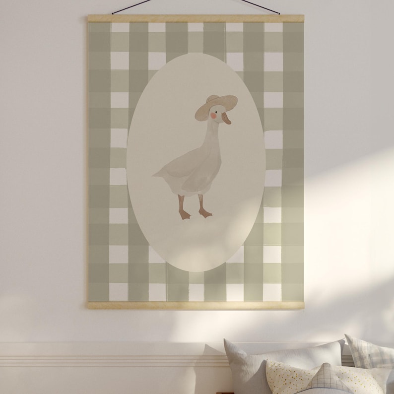 May include: A wall hanging with a watercolour illustration of a goose in a hat, set against an oval backdrop. The background is a green and white checked pattern. It is suspended by a wooden rod and black string.
