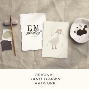 May include: A still life arrangement with a watercolour illustration of a goose in a hat, a logo for "EM Atelier Co Home Prints", a paintbrush, paint samples, and the text "ORIGINAL HAND-DRAWN ARTWORK". The scene is set on a neutral-toned fabric.