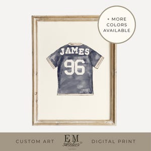 May include: Watercolor print of a navy blue jersey with the name "JAMES" and the number "96" in white. The artwork is framed in a light-colored wooden frame. Text on the image reads "+ MORE COLORS AVAILABLE", "CUSTOM ART", and "DIGITAL PRINT".
