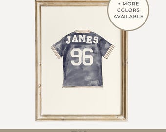 May include: Watercolor print of a navy blue jersey with the name "JAMES" and the number "96" in white. The artwork is framed in a light-colored wooden frame. Text on the image reads "+ MORE COLORS AVAILABLE", "CUSTOM ART", and "DIGITAL PRINT".