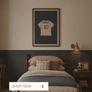 May include: A framed poster featuring a soccer jersey with "MESSI 10" on a dark background hangs above a bed with a patterned comforter. The room has a warm, inviting aesthetic, with a bedside table and a wall-mounted lamp. Text on the image reads "Sports Wall Art, Custom Posters for Kids."