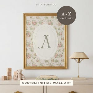 May include: A framed floral print with the letter "A" in a decorative oval. The print has a gold frame and a background of pink roses. The text "CUSTOM INITIAL WALL ART" is at the bottom.