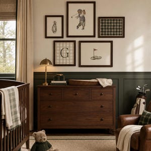 May include: A golf-themed nursery with framed artwork, a dark wood dresser, a cot, and a leather armchair. The artwork includes golf illustrations and a plaid pattern. A teddy bear sits on the floor near books. The room's colour scheme includes brown, green, and cream.