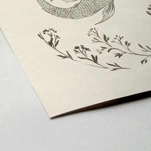May include: A black and white illustration of a mermaid tail with a floral design around it. The background is a light beige.