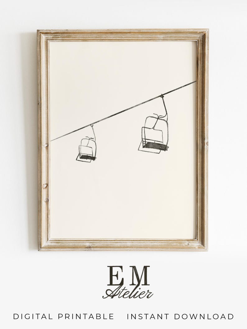 May include: A framed print with a minimalist line drawing of two ski lift chairs hanging from a cable. The artwork is in black and white, set against a cream background. The frame is light, distressed wood. The text "EM Atelier" and "DIGITAL PRINTABLE INSTANT DOWNLOAD" are at the bottom.