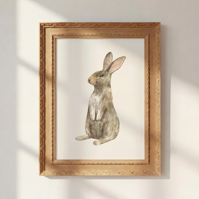 May include: A framed watercolor painting of a brown rabbit sitting upright in profile. The rabbit has long ears, a light-colored chest, and textured fur. The artwork is enclosed in a rectangular, ornate, light brown wooden frame with carved edges.