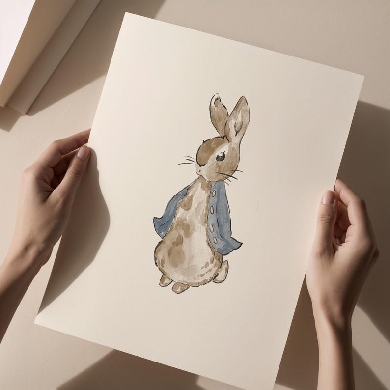 May include: Watercolor illustration of a rabbit wearing a blue jacket. The rabbit is depicted in shades of brown and tan, with a light blue jacket. The artwork is on a cream-colored paper, held by hands.