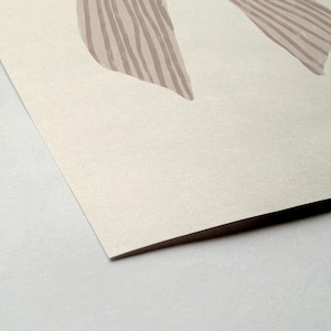 May include: Abstract art print featuring two beige shapes with vertical striped details on a cream-colored background. The artwork is presented on a textured paper, with a visible corner and a white surface.
