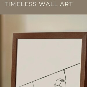 May include: A framed minimalist ski print. The artwork features a black and white line drawing of two ski lift chairs on a neutral background, set within a dark brown wooden frame.