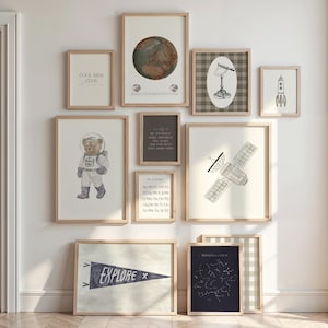 Peut inclure: Une collection d'impressions d'art encadrées sur le thème de l'espace et de l'exploration. Les impressions incluent un globe, un ours en peluche astronaute, une fusée, un satellite et le mot "EXPLORE". Les cadres sont en bois clair.