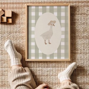 May include: A framed print with a charming illustration of a goose in a hat. The goose is set against an oval backdrop on a green and white gingham background. The frame is made of light-coloured wood.