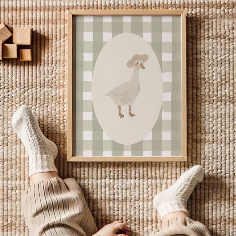 May include: A framed print with a charming illustration of a goose in a hat. The goose is set against an oval backdrop on a green and white gingham background. The frame is made of light-coloured wood.