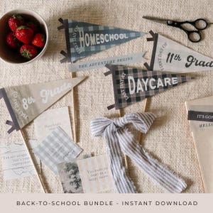 May include: A collection of back-to-school themed pennant flags, cards, and a bow. The flags read "Homeschool", "8th Grade", "11th Grade", and "Daycare". The cards have inspirational quotes. A bowl of strawberries and scissors are also present.