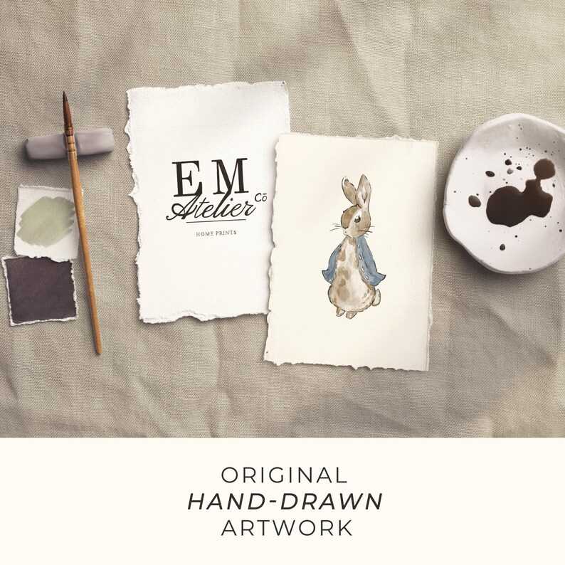 May include: Watercolor artwork featuring a bunny in a blue jacket, a paint brush, and a small dish with paint. The artwork is on textured paper with the text "EM Atelier co HOME PRINTS". The image is on a neutral linen background.