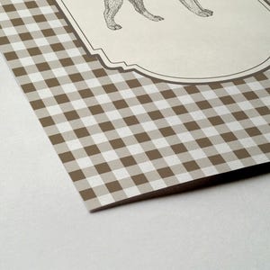 Pu&ograve; includere: Vista angolare di un prodotto di carta con un motivo a quadri marrone e bianco. Una sezione color crema presenta un'illustrazione dettagliata delle zampe di un animale. La carta &egrave; angolata, rivelando una superficie bianca sottostante.