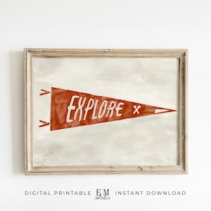 May include: A framed print featuring a red pennant with the word "EXPLORE" in white. The pennant has a small white "X" and is set against a light gray watercolor background. The frame is a light brown color.