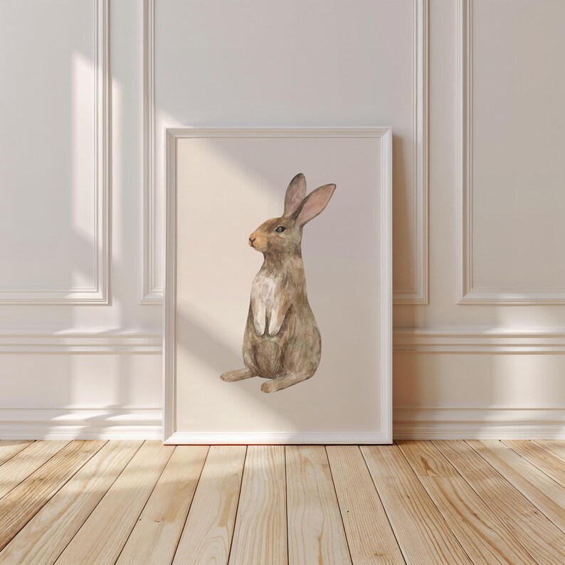 May include: A framed wall art print featuring a watercolor illustration of a brown rabbit sitting upright in profile. The rabbit has long ears, a light-colored chest, and soft fur textures. The artwork is displayed in a simple white frame.