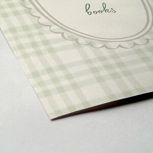 May include: A light green and white plaid pattern with the word "books" in a handwritten font. The text is inside a decorative oval frame with a scalloped edge. The paper has a slight angle.