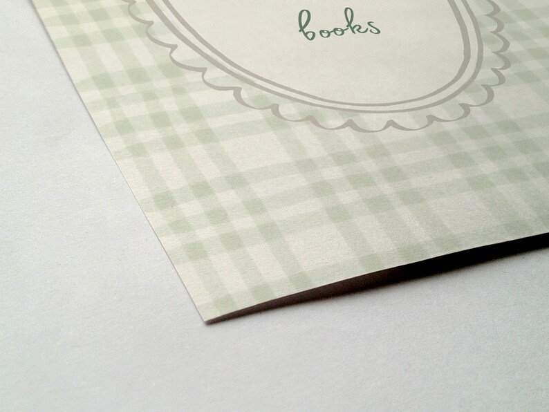 May include: A light green and white plaid pattern with the word "books" in a handwritten font. The text is inside a decorative oval frame with a scalloped edge. The paper has a slight angle.