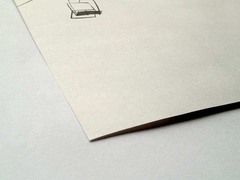 May include: A close-up of a corner of a piece of paper with a sketch of a chair in the upper right corner. The paper is off-white and has a slight texture. The edge of the paper is dark.