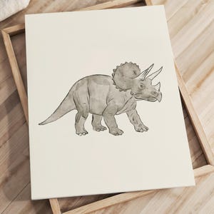 May include: A grayscale illustration of a Triceratops dinosaur on a cream-colored background. The artwork is framed in a light-colored wooden frame. The dinosaur is depicted in a walking pose, with its distinctive frill and horns clearly visible.