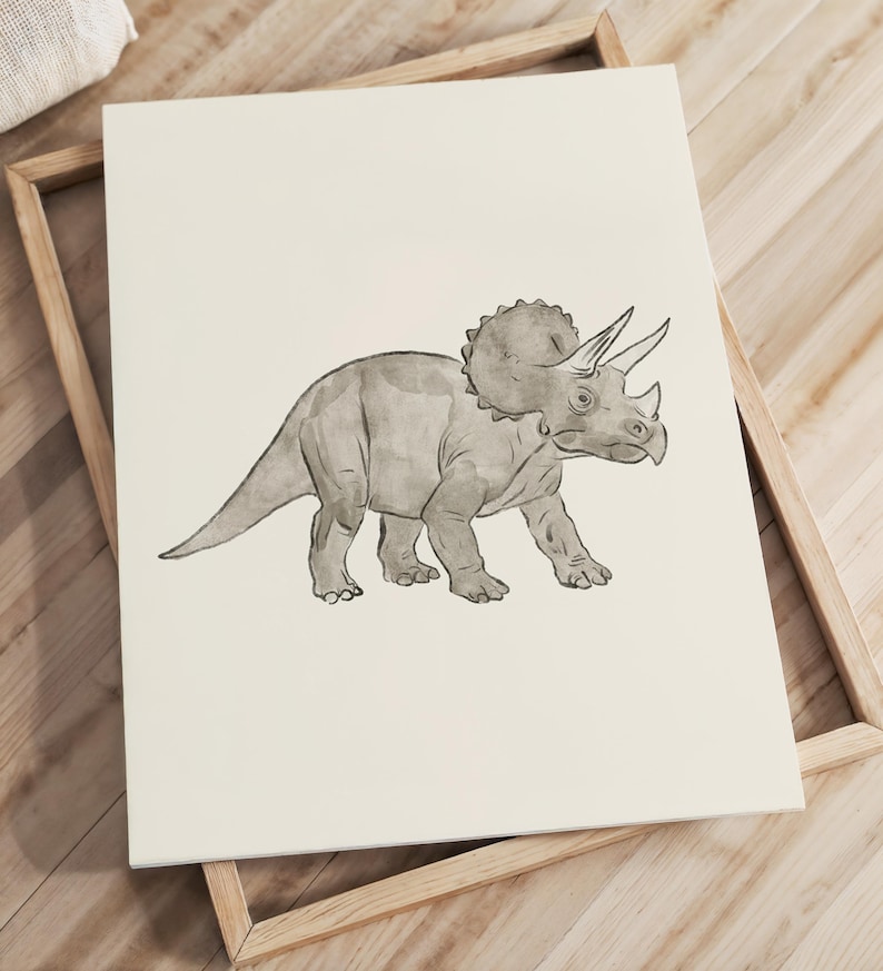 May include: A grayscale illustration of a Triceratops dinosaur on a cream-colored background. The artwork is framed in a light-colored wooden frame. The dinosaur is depicted in a walking pose, with its distinctive frill and horns clearly visible.