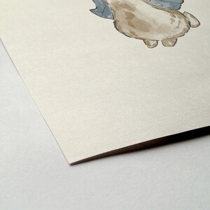 May include: Watercolor illustration of a whimsical creature with a light brown body, gray wings, and small feet. The artwork is on textured, off-white paper, with a corner of the paper visible in the foreground. The style is soft and illustrative.