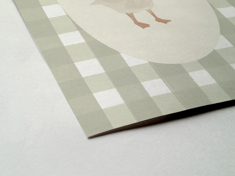 May include: A printed card with a light green and white gingham pattern. A light beige oval shape with a goose illustration is in the upper right corner. The goose's feet are visible. The card's corner is in focus.