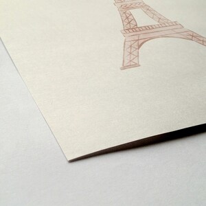 May include: A watercolor illustration of the Eiffel Tower in a soft, muted pink hue. The artwork is on a textured, off-white paper, with the tower's architectural details visible. The image is a close-up, focusing on the tower's structure.