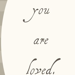 Może przedstawiać: Kremowe tło z napisem "you are loved" w eleganckim, ciemnobrązowym skrypcie. Tekst jest wyśrodkowany, z miękkim, zakrzywionym elementem projektu po lewej stronie.