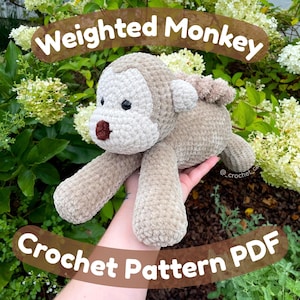 May include: A crocheted monkey in shades of tan and cream, with a brown nose and black eyes. The text "Weighted Monkey Crochet Pattern PDF" is displayed on the image. The monkey is lying on a hand.