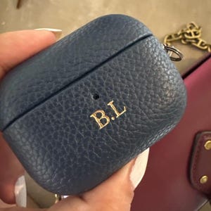 May include: A blue leather Airpods case with a gold chain and the initials "B.L." embossed on the front.