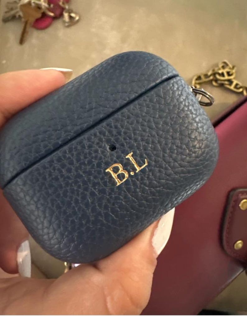 May include: A blue leather Airpods case with a gold chain and the initials "B.L." embossed on the front.