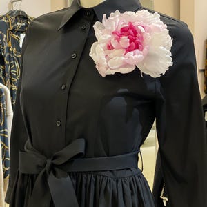 May include: A black dress with a large pink flower brooch, a black sash, and long sleeves.