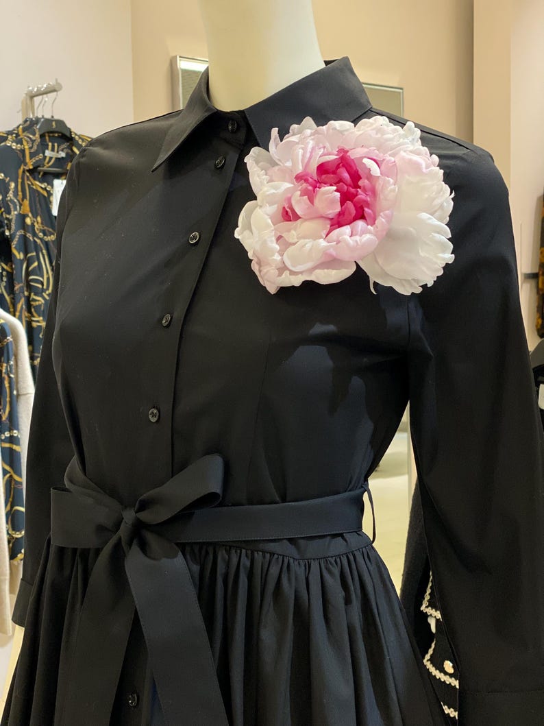 May include: A black dress with a large pink flower brooch, a black sash, and long sleeves.