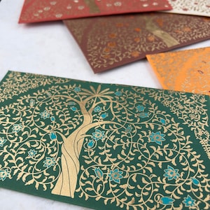 May include: A green envelope with a gold tree and blue flowers design. The envelope is decorated with a intricate floral pattern.