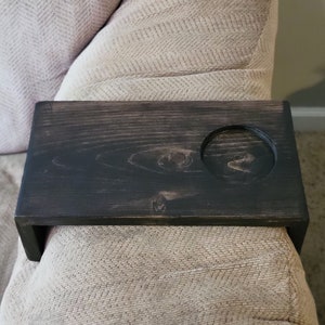 May include: A dark wood armrest tray with a circular cutout for a cup or glass. The tray is attached to a beige couch.
