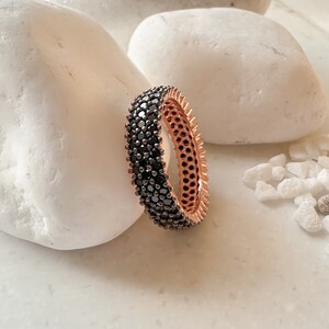 May include: A rose gold band ring with a black pave setting. The ring is made of metal and has a smooth finish.