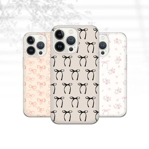 Könnte beinhalten: Drei Handyhüllen mit verschiedenen Mustern. Die erste Hülle hat ein rosa-weißes Schleifenmuster. Die zweite Hülle hat ein schwarzes Schleifenmuster auf beigefarbenem Hintergrund. Die dritte Hülle hat ein Blumenmuster mit rosa und weißen Blumen.