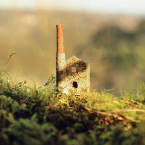May include: A miniature model of a stone building with a red and white chimney. The building is surrounded by green moss.